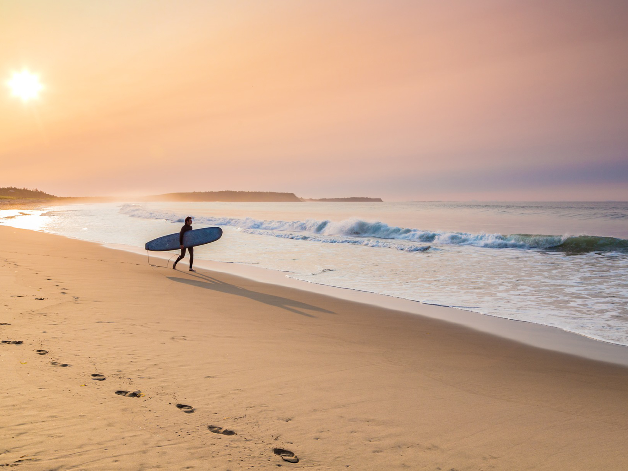 Surfer walking the beach at sunset, Nova Scotia